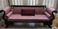 Front angle view of Victorian mauve brocade roll-arm sofa showing single seat cushion, two bolster pillows, and carved wooden arms with lion's foot base.