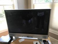 Front view of the silver-frame 42-inch Panasonic Viera plasma TV powered off, standing on its silver stand with remote control placed on the right side.