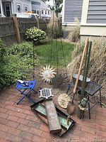 Overall photo of landscaping and garden decor items outside on brick patio and greenery background, including copper liners, metal decor, tools, and stools.