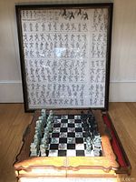 Framed Tai Chi poster on wall with carved wooden chess set displayed with patterned resin chess pieces set up on the board.
