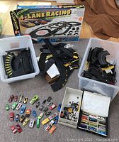 Full view of TYCO 4 Lane Racing box with loose racing track parts, chassis, and multiple small cars laid out