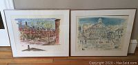 Two framed artwork prints by Birdsong depicting Boston scenes, Faneuil Hall and Back Bay rowhouses, in cream mattes and gold-tone frames, leaned against wall on wooden floor.