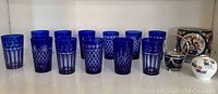 Photo of 12 cobalt blue cut glass tumblers with 3 distinct cut patterns showing clear reveals in the glass