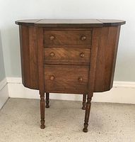 Front view of the closed sewing table showing the three drawers and side compartments in closed position.