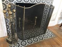 Front view of brass-fireplace screen with andirons and tools arranged inside fireplace.