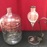 Photo showing full lot including large clear glass water jug and wrought iron absinthe drip decanter with decorative base.