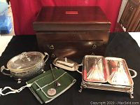 Photo showing wooden silverware storage box, oval glass casserole and rectangular double casserole in silver plate baskets, butter dish, silver snuffer, and anti-tarnish bags