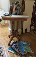 Photo of antique Eastlake parlor table with white marble top on oak stand, holding travel books with wooden bookends and board coasters on the tabletop.