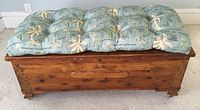 Front view of the Forest Park cedar chest with Tommy Bahama cushion on top, showing wood finish, cushion pattern, and brass accents.