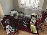 Wide view of assorted Christmas decorations laid on red fabric including wreaths, candles, ceramic dishes, gift boxes, and decorative figurines.