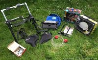 Photo of all items together on grass including helmet boxes, bags, rack, seat covers, bicycle lock, and cables