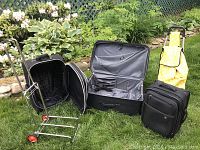 Wide view of all items in lot placed on grass, showing dollies and suitcases opened and closed