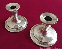 Pair of silverplate on copper candlesticks shown upright on red fabric background, highlighting the design and finish.
