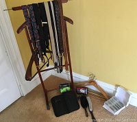 Wooden valet stand holding ties and belts, with grooming brushes, voltage converter, coin dish, hangers and boxes on floor