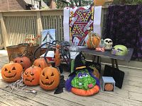 Photo showing illuminated orange plastic pumpkins with carved faces, spider decoration, green monster plush pumpkin with witch hat, decorative skull, and green glittery monster helmet.