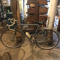 Full side view of medium blue Peugeot road bike with carrier rack and water bottle holder, showing frame and tires.
