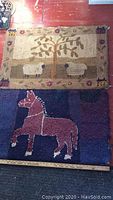 Two antique hooked matts on red wooden floor. One with sheep under a tree; other with a horse graphic.
