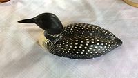 Top side view of hand painted wooden loon showing black body with white spots and red eyes.