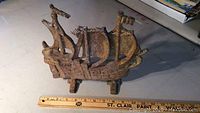Side view of rusty cast iron ship figurine with ruler for scale showing about 10 inches length