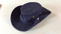Navy blue Tilley hat with wide brim and brass hardware, shown from the side angle.