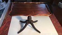 Full view of the antique Duncan Phyfe style tilt top side table showing scalloped rectangular wooden top and tripod base with brass feet.