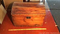 Front view of wooden humpback trunk with curved lid placed on wooden floor with a tape measure for size reference.