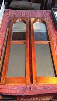 Top-down view of both wooden window frames with mirror inserts placed side by side on a patterned fabric surface.