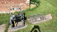 Full view of gray Yard Works hose reel next to rolled metal tomato cages on ground near brick wall.
