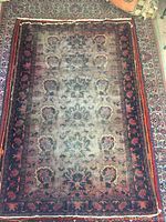 Top view of rectangular vintage area carpet with large central medallion and floral pattern, colors faded and worn in center with darker decorative border.