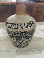 Front view of beige glazed stoneware jug with black text 'Cruiskeen Lawn Mitchell's Old Irish Whiskey' and decorative crown illustration.