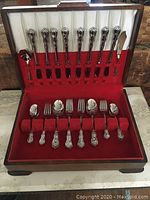 Full wooden case with cutlery for eight, showing knives, forks, spoons, and serving utensils organized inside fitted slots.