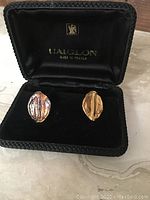 Front view of two cuff links inside original black box, showing gold-tone and silver-tone textured design with vertical groove detail. Box interior bears L'Aiglon logo and 'Made in France' text.