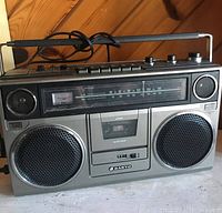 Front view of the Sanyo boom box showing speakers, controls, cassette mechanism, and antenna.