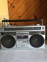 Front view of vintage Sanyo M9860 boom box showing dual speakers, cassette player with visible tape, and control panel.