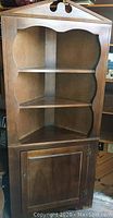 Front view of vintage wood corner cabinet showing the upper three scalloped-edge shelves and lower closed cabinet section with door and hardware.