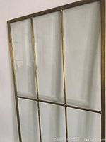 Front view of large rectangular glass panel framed by brass with vertical and horizontal brass bars creating grid sections.