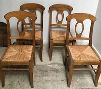 Four solid wood dining chairs with rush seats arranged in storage room against white wall