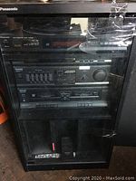 Photo of black wooden cabinet housing entire Panasonic stereo system including CD player, amplifier, cassette deck, with glass door showing the components inside.