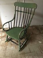 Full view of antique green painted wooden rocking chair with black vertical spindles, curved armrests, and turned legs on rocker rails.