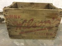 View of one side showing faded 'Drink Wilson's Ginger Ale' branding in red on wooden slats with weathered finish.