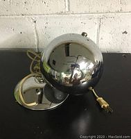 Front view of the vintage chrome spherical lamp with attached power cord and round base on a black surface.