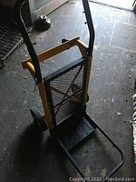 Front angled photo of the metal moving cart showing handle bars, foldable base platform and mesh back support.