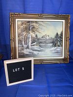 Front view of large ornate framed winter cabin painting showing overall condition and setting with lot sign