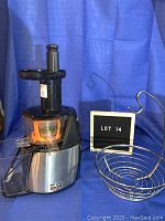 Photo of Salton VitaPro juicer next to metal fruit basket with hook, against blue background.