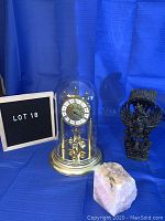 Full lot view showing gold colored clock under glass dome, rose quartz crystal on right side, and carved wood figurine on far right.