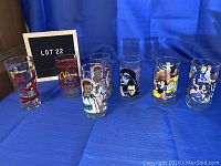 Seven collectible glasses displayed on blue cloth with framed sign 'LOT 22'