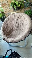 Front view of the round chair showing tan cushioned fabric seat with some stains and metal frame base