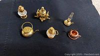 Six miniature kitchen items including two brass lanterns, a brass coffee grinder, a brass teapot, a smaller brass kettle, and a miniature oil lamp.