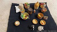 Top-down photo showing a variety of miniature dollhouse kitchen food and accessories arranged on a dark cloth.