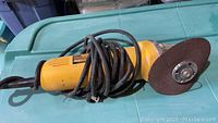 Side view of yellow Dewalt DW818 angle grinder with attached grinding disc and wrapped power cord.